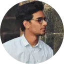 Portrait of a young man wearing sunglasses, looking to the side outdoors with a blurred stone wall background, emphasizing modern style and personal branding for digital identity solutions.