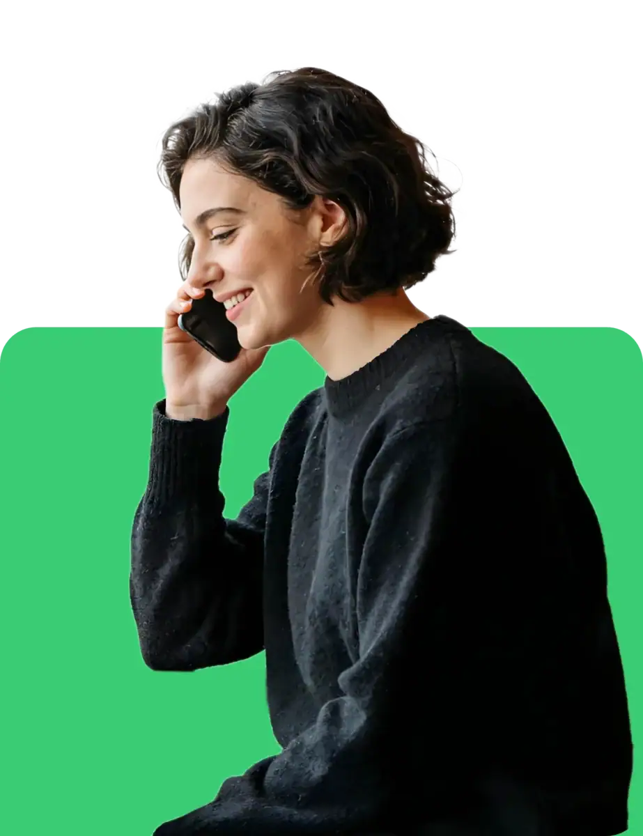 A young woman with short, dark hair smiling while talking on her mobile phone. She is dressed in a black sweater and appears happy and engaged in her conversation, with a modern, vibrant background.