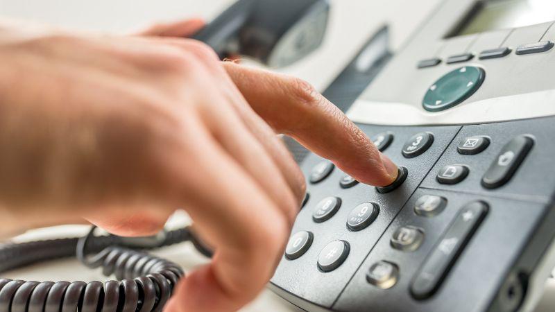 Close-up of a hand dialing a phone number on a modern office phone, illustrating how to buy a phone number online through 2Number.