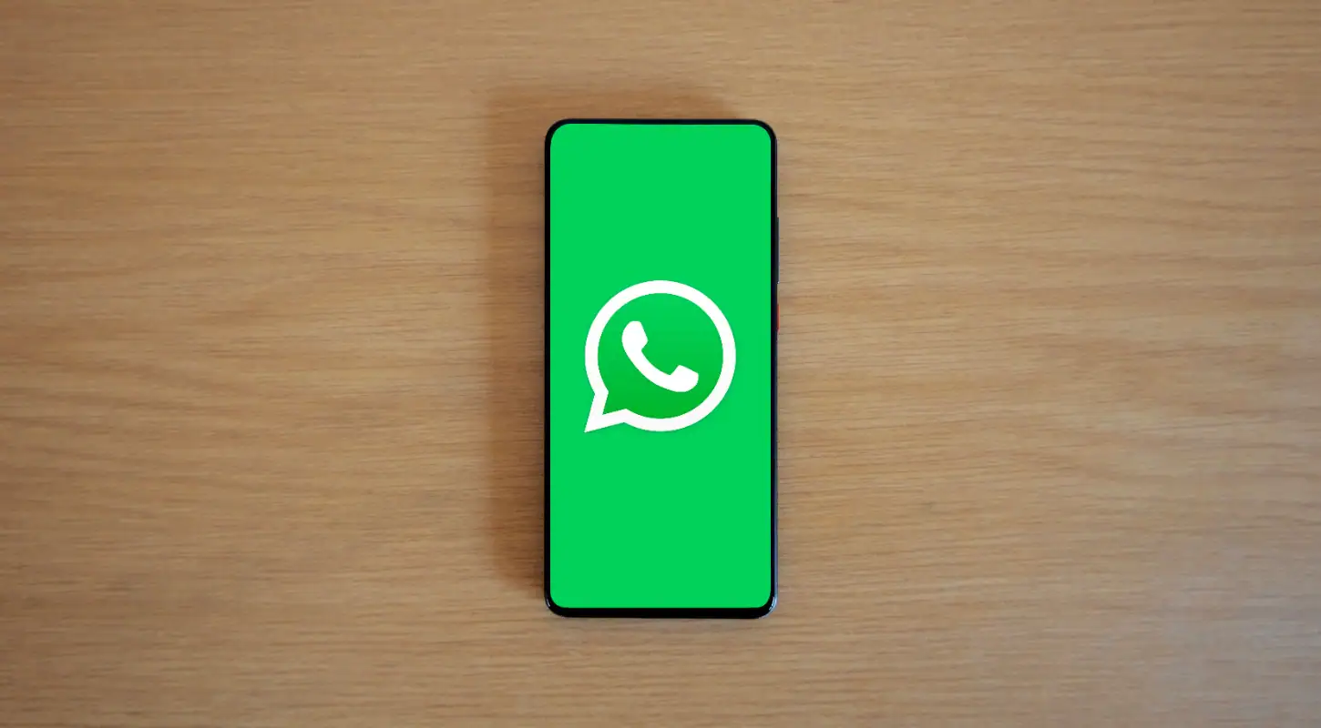 Smartphone displaying the WhatsApp logo on a wooden surface, representing messaging app communication.