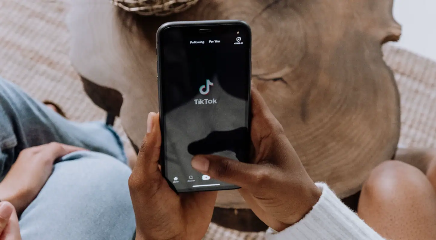 Person holding a smartphone displaying the TikTok app, with a wooden table in the background.