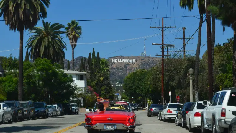 View of Hollywood Sign in Los Angeles with palm trees, cars, and power lines on a sunny day.