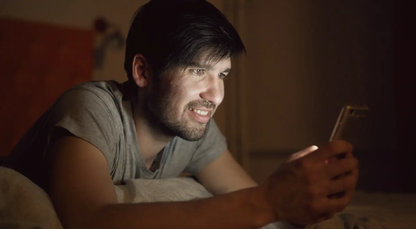Man looking at his smartphone with a worried expression in a dimly lit room, emphasizing privacy concerns.